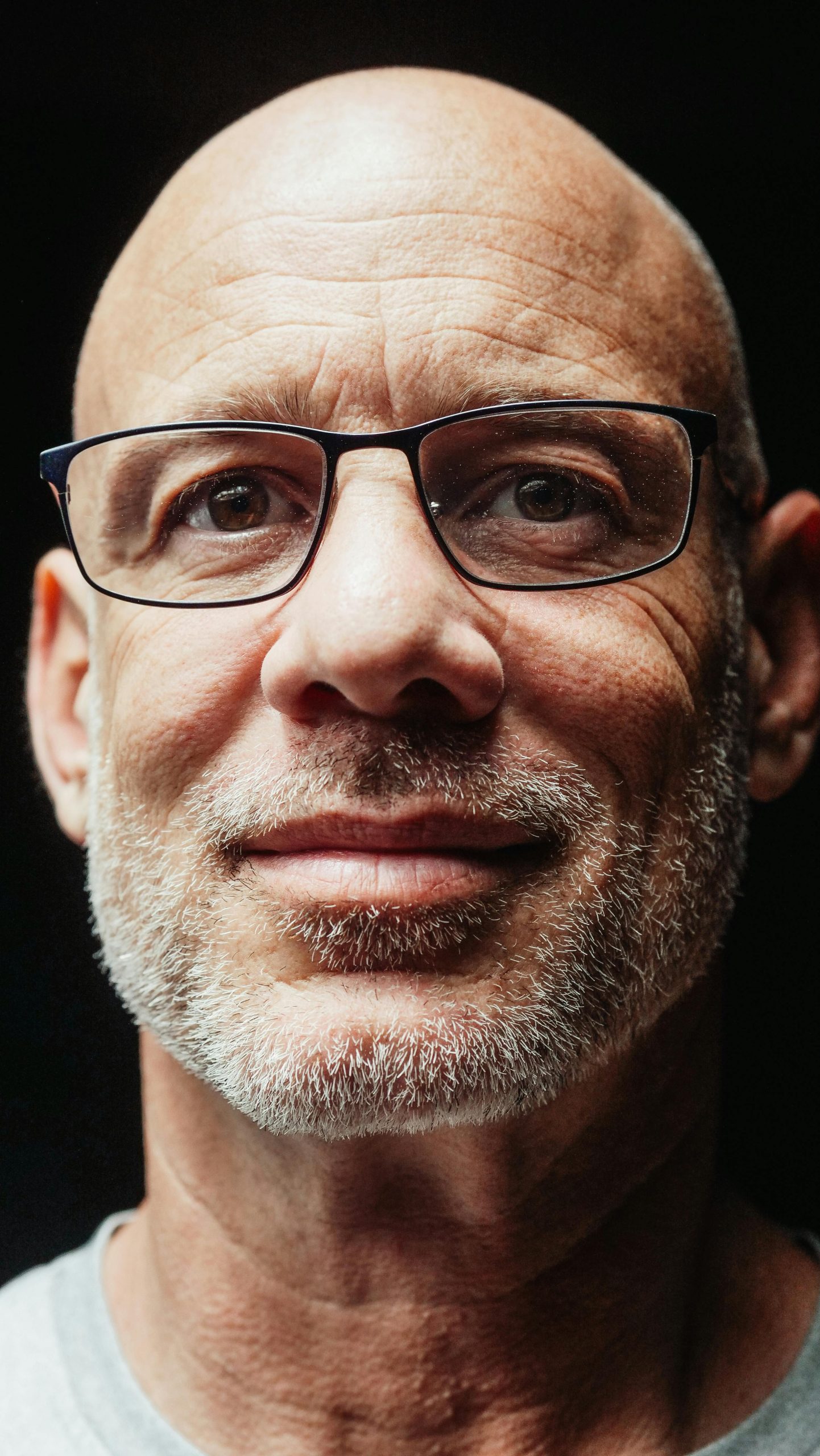 Close-up portrait of a bald mature man wearing glasses, looking confidently at the camera.